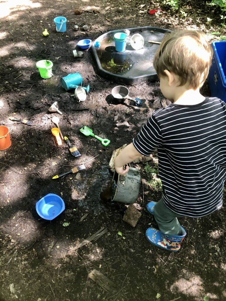 Little boy playing with a mud kitchen outdoors.